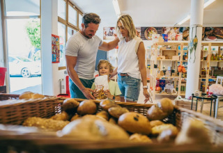 Gezin koopt brood bij de bakker in een vakantiepark met glampingverblijven.