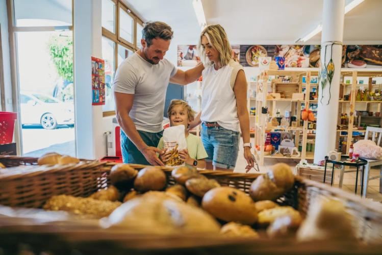 Gezin koopt vers brood bij de bakker in een vakantiepark met glampingaccommodatie.