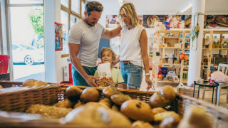 Gezin koopt vers brood bij de bakker in een vakantiepark met glampingaccommodatie.