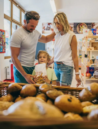Familia compra pan fresco en la panadería de un parque vacacional que ofrece alojamientos glamping.