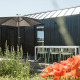 Udsigt over en træterrasse med parasol, bord og stole ved tiny house Scandic i De Klepperstee, Holland.