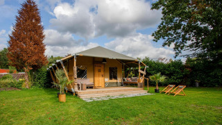 Safari tent Cottage Kaa at Camping Vossenberg in the Netherlands with deck, chairs, and garden view.