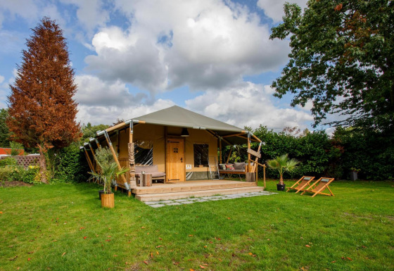 Tienda Safari Cottage Kaa en Camping Vossenberg, Países Bajos, con terraza, sillas y jardín verde.