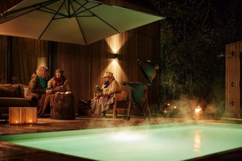 Tres personas disfrutan junto a la piscina y sauna por la noche en Unbrick One | Sauna and Pool en Brinckerduyn, Países Bajos.