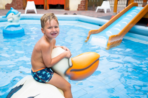 Jongen in zwembroek op grote vogel in kinderbadje met glijbaan bij vakantiepark in Utrecht, Nederland.