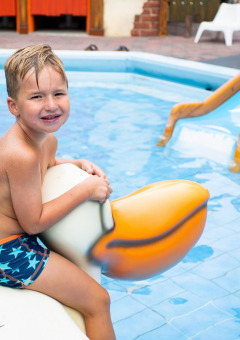 Niño en bañador montando una figura de pájaro grande en una piscina infantil con tobogán en Utrecht.