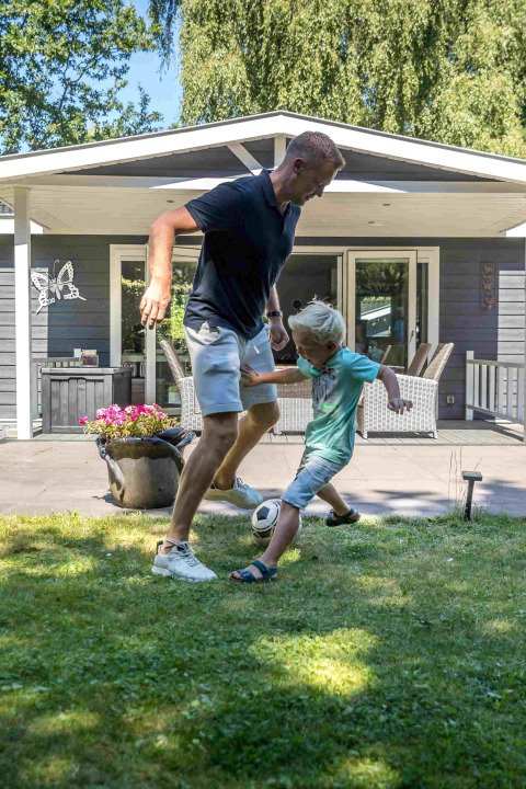 Padre e hijo juegan al fútbol sobre el césped frente a una cabaña en De Thijmse Berg, un parque vacacional en Utrecht.