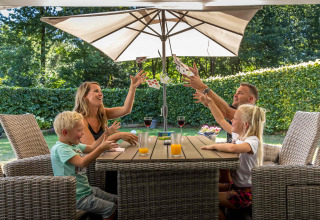 A family playing cards together outdoors under a parasol at De Thijmse Berg holiday park in Utrecht.