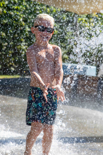 Jongen met zonnebril speelt in de watersproeiers op vakantiepark De Thijmse Berg in Utrecht, Nederland.