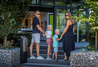 A family of four holds hands outside De Thijmse Berg holiday park in Utrecht, Netherlands, smiling back.