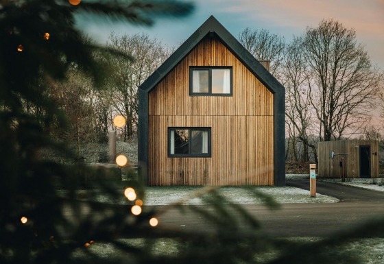 Moderno chalet in legno Unbrick One con sauna, circondato da alberi e neve, visto attraverso le luci.