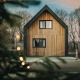 Moderne træhytte Unbrick One med sauna, omgivet af træer og sne, set gennem juletræ og lys.