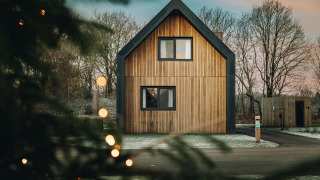 Moderna cabaña de madera Unbrick One con sauna, rodeada de árboles y nieve, vista entre luces.