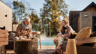 Ouder koppel geniet buiten van wijn en hapjes bij Unbrick One lodge met sauna en zwembad.