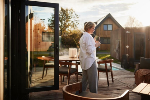 Vrouw ontspant met een drankje op het terras bij Unbrick One | Sauna en Zwembad bij Brinckerduyn, Nederland.