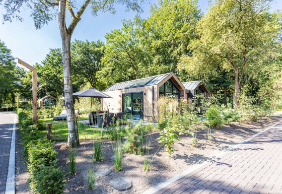 Casa pequeña Lodge Royal Eco en Résidence Lage Vuursche, Países Bajos, rodeada de árboles y vegetación verde.