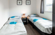 Habitación con dos camas individuales, mesa de noche, lámpara y arte en Berkenhoeve, Résidence Lichtenvoorde, Países Bajos.