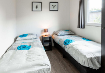 Chambre avec deux lits simples, table de chevet, lampe et décoration murale à Berkenhoeve, Résidence Lichtenvoorde, Pays-Bas.