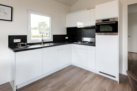 Cucina moderna bianca con piani neri, forno e piano cottura nella lodge Berkenhoeve presso Résidence Lichtenvoorde nei Paesi Bassi.