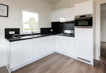 Cucina moderna bianca con piani neri, forno e piano cottura nella lodge Berkenhoeve presso Résidence Lichtenvoorde nei Paesi Bassi.
