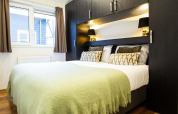 Soveværelse med dobbeltseng, grøn plaid, moderne sorte skabe og vindue på Berkenhoeve Wellness i Holland.