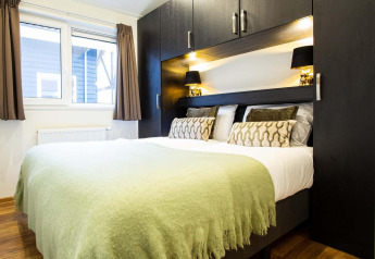 Slaapkamer met dubbelbed, groene plaid, zwarte kasten en raam in Berkenhoeve Wellness, Nederland.