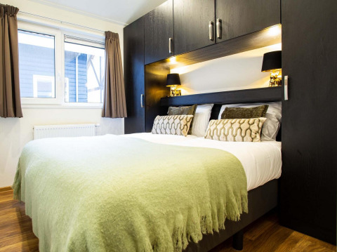 Bedroom with double bed, green throw, modern black cabinets and window at Berkenhoeve Wellness in the Netherlands.