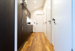 Modern hallway with wooden floor, white doors and dark kitchen at Berkenhoeve Wellness, Résidence Lichtenvoorde.