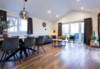 Moderne woon- en eetruimte met parketvloer, grote ramen en stijlvolle meubels in Berkenhoeve Wellness lodge.