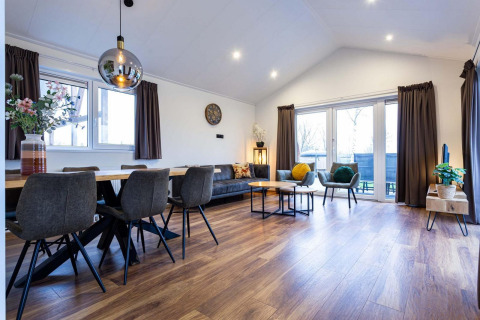 Moderne woon- en eetruimte met parketvloer, grote ramen en stijlvolle meubels in Berkenhoeve Wellness lodge.