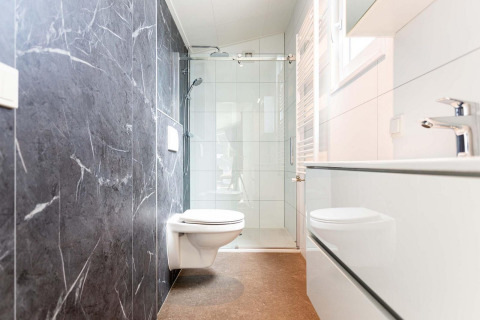 Moderne badkamer bij een glamping-accommodatie met wandcloset, douche en stijlvolle zwart-witte tegels.