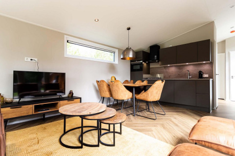 Alojamiento glamping moderno y luminoso con cocina abierta, comedor, sala de TV y muebles de madera.