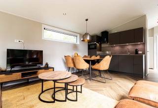 Alojamiento glamping moderno y luminoso con cocina abierta, comedor, sala de TV y muebles de madera.