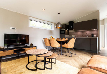 Alojamiento glamping moderno y luminoso con cocina abierta, comedor, sala de TV y muebles de madera.