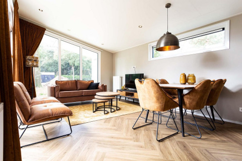 Elegante soggiorno glamping con arredi in pelle marrone, tavolo da pranzo e grandi finestre sulla natura.