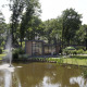 En smuk lodge ved en dam med springvand i Landgoed de Scheleberg, Nederlandene, omgivet af træer.