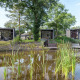 Moderne lodges ved Landgoed de Scheleberg i Holland, placeret ved en dam og omgivet af grønne træer.