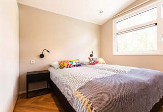 Camera da glamping luminosa con letto grande, cuscini colorati, lampade nere e ampia finestra.