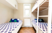 Habitación de glamping moderna con literas, ropa de cama colorida y paredes claras junto a una ventana central.