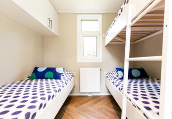 Habitación de glamping moderna con literas, ropa de cama colorida y paredes claras junto a una ventana central.