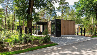 Moderna cabaña en Veluwe Hoeve, Resort Veluwe en los Países Bajos, rodeada de árboles y vegetación.