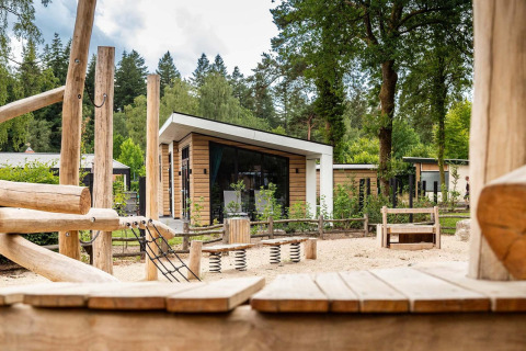 Área de juegos de madera natural frente a la lodge Silva en Resort Veluwe, Países Bajos, rodeada de árboles.