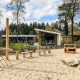 Legeplads med sand, træklatrestativ og moderne lodge i baggrunden på Resort Veluwe, Nederlandene.