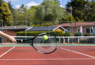 A hand hits a tennis ball with a racket on an outdoor court at Bungalowpark Het Verscholen Dorp holiday park.