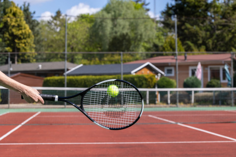 Een hand slaat een tennisbal met een racket op een buitenbaan bij Bungalowpark Het Verscholen Dorp.