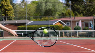 Una mano golpea una pelota de tenis con una raqueta en la pista exterior de Bungalowpark Het Verscholen Dorp.