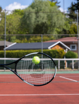 Een hand slaat een tennisbal met een racket op een buitenbaan bij Bungalowpark Het Verscholen Dorp.