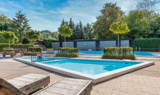 Buitenzwembad met ligstoelen en groen bij Bungalowpark Het Verscholen Dorp in Gelderland, Nederland.