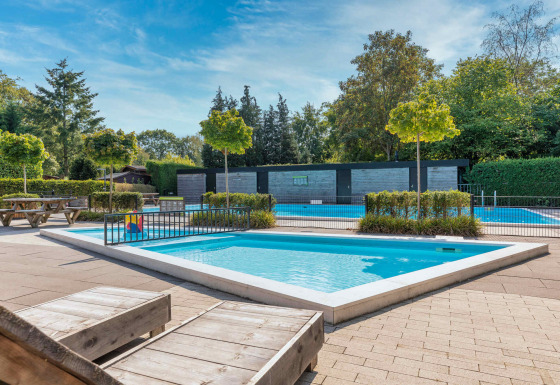 Außenpool mit Liegestühlen und Bäumen im Bungalowpark Het Verscholen Dorp, Gelderland, Niederlande.
