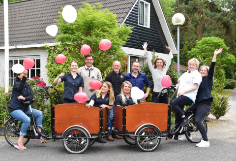Grupo celebrando con globos y bicicletas frente a Bungalowpark Het Verscholen Dorp, Gelderland, Países Bajos.